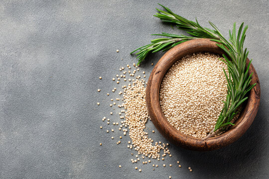White raw organic quinoa in wooden bowl and rosemary on grey background. Healthy food ingredients. 