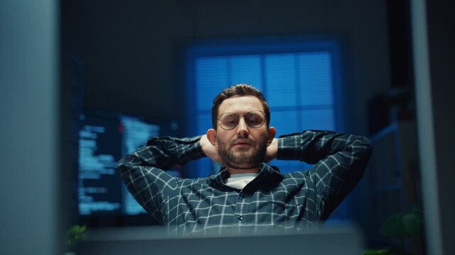 Tired male developer stretches arms to release stress from heavy workload in office at night. Employee burnout relief and recovery, Workplace health care, Rested mind for better productivity concept.