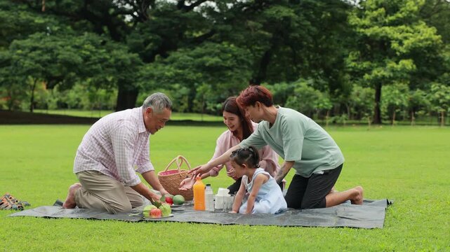 Happy Asian family having fun time on picnic at city nature park sunny day, outdoor activitie with daughter father, mother and grandfather