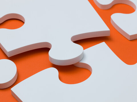 White Jigsaw Puzzle Pieces Fitting Together on Orange Background Representing Solution and Teamwork Concept