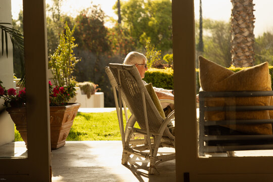 profile of elderly man relaxing in chair at sunset framed through windows