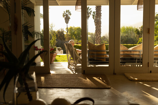 profile of elderly man relaxing in chair at sunset framed through windows