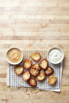 Golden potato latkes draining on a wire rack with apple sauce and soured cream above