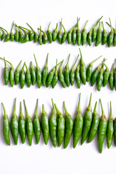 Organized horizontal rows of fresh green bird's eye chilies or cabe rawit hijau on white background