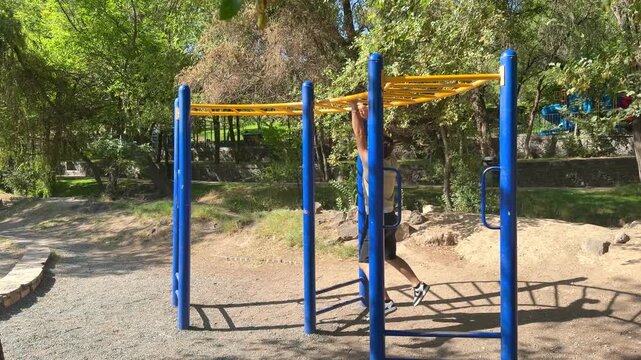 Man exercising on monkey bars outdoors in a sunny park, fitness and calisthenics workout