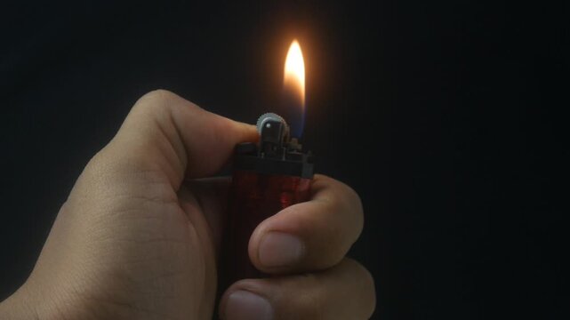 Hand holding a burning gas lighter with a small flame on a dark background