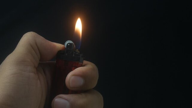 Hand holding a burning gas lighter with a small flame on a dark background