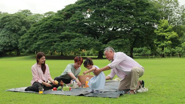 Happy Asian family having fun time on picnic at city nature park sunny day, outdoor activitie with daughter father, mother and grandfather