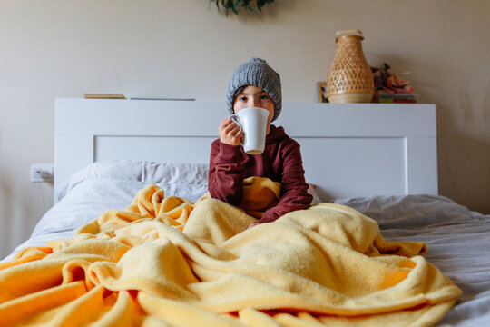 Portrait of Child Drinking Hot Drink in Bed, Feeling Cold at Home
