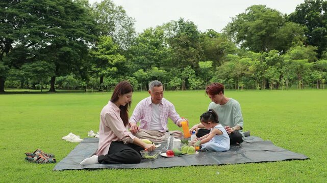 Happy Asian family having fun time on picnic at city nature park sunny day, outdoor activitie with daughter father, mother and grandfather