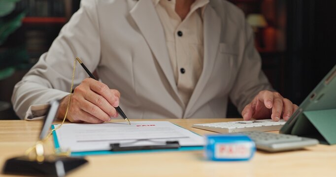 Accountant signs financial invoice after payment review, ensuring each invoice reflects clear payment terms before stamping invoice paper.