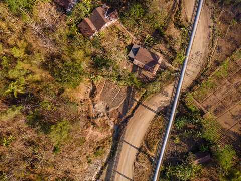 Aerial Scenery of Covered Conveyor Belt System with Checkpoint Buildings and a Service Road Crossing Hilly Terrain in Indonesia. Industrial Infrastructure Extends Across the Green Hillside. 