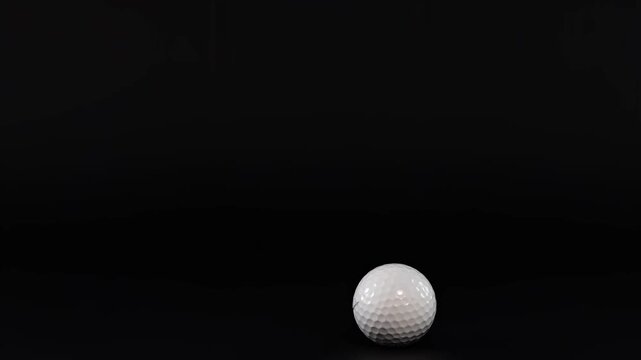 White golf ball falling and bouncing on black surface in slow motion against dark background.