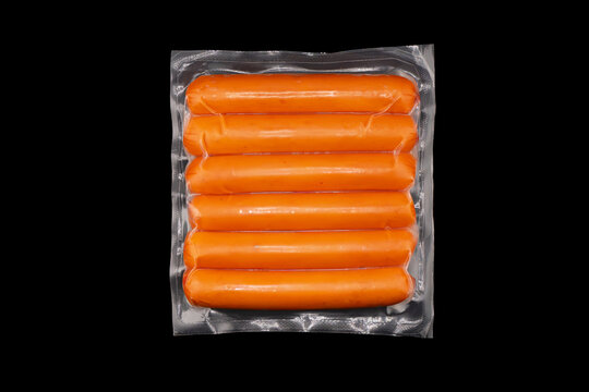 Sausages in vacuum plastic packaging isolated on black background. Vacuum transparent packaging with fresh sausages. A pack of sausages in a vacuum isolated.