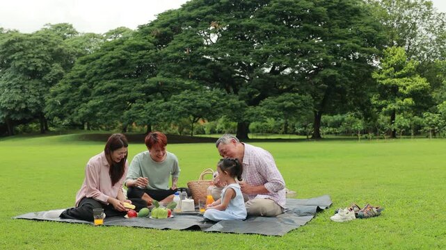 Happy Asian family having fun time on picnic at city nature park sunny day, outdoor activitie with daughter father, mother and grandfather
