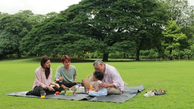Happy Asian family having fun time on picnic at city nature park sunny day, outdoor activitie with daughter father, mother and grandfather