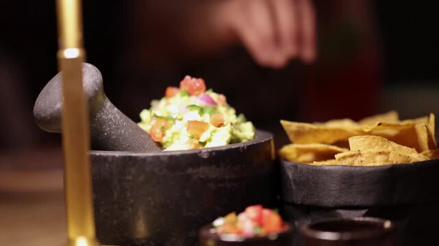 Mexican appetizers with fresh guacamole in stone mortar and crispy corn tortilla chips at dark restaurant.