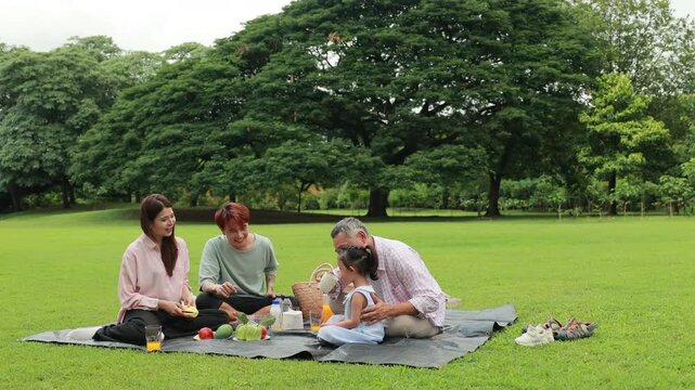 Happy Asian family having fun time on picnic at city nature park sunny day, outdoor activitie with daughter father, mother and grandfather