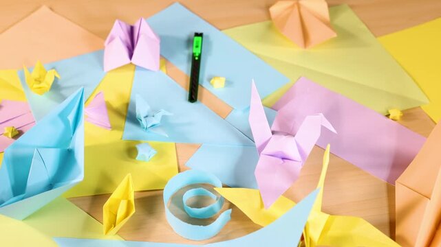 Creative mess with various colorful origami paper figures and stationery on wooden desk background.