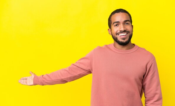 Young latin man isolated on yellow background extending hands to the side for inviting to come