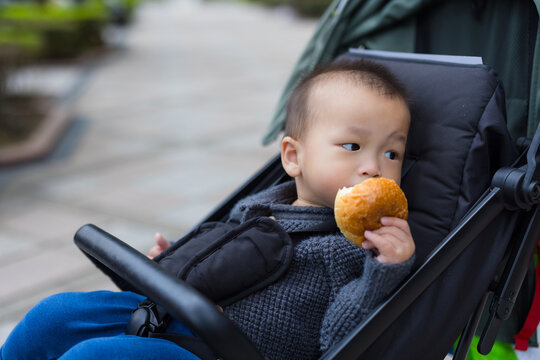 Cute toddler eating bread snack sitting in stroller pram
