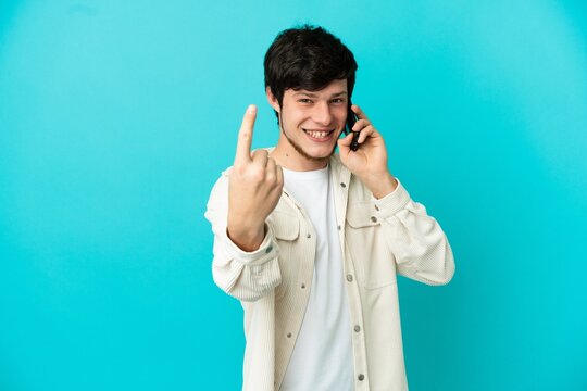 Young Russian man using mobile phone isolated on blue background doing coming gesture