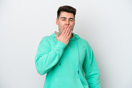 Young caucasian man isolated on white background yawning and covering wide open mouth with hand