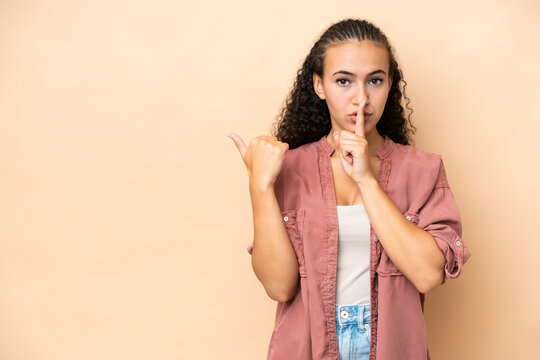 Young woman isolated on beige background pointing to the side and doing silence gesture