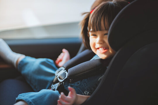 Happy toddler girl safely secured in child car seat with safety harness inside vehicle, smiling during family journey, road travel, transportation.