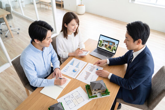 住宅購入の資金計画を相談する若い夫婦と不動産営業担当者の商談風景｜不動産・住宅ローンのイメージ