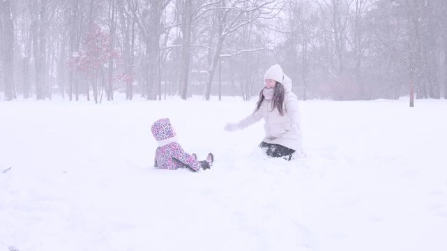 Child outdoor winter. Toddler sitting and playing in snow with mother. Family bonding concept.