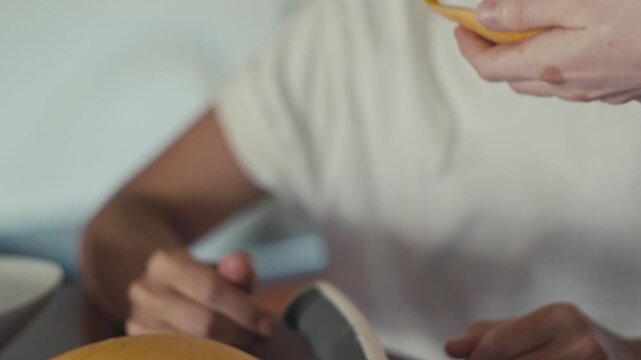 Two people sharing ripe juicy mango piece on metal fork with friendly smiles in warm indoor kitchen close-up with hands offering tasting bite under soft light glow