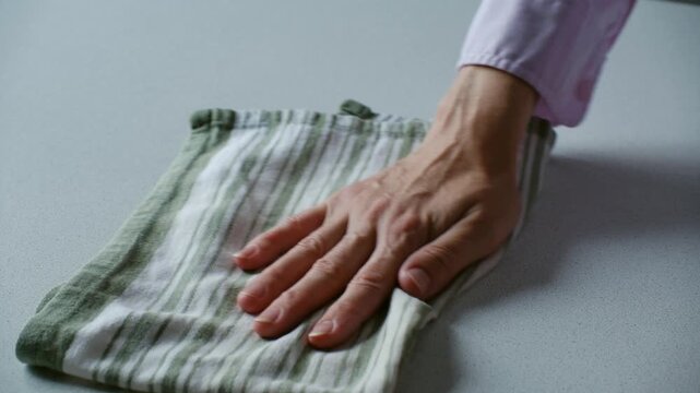 Female hand meticulously wiping clean kitchen counter with a striped cloth, performing daily household chores and ensuring a spotless, hygienic surface for a healthy living environment