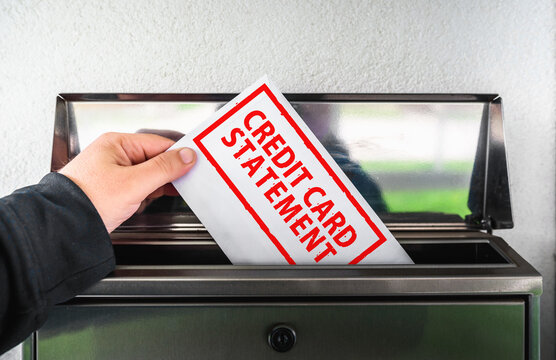 Hand putting an envelope with a credit card statement text into a mailbox