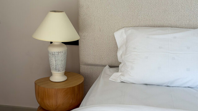 Cozy modern bedroom detail with white bedding, upholstered headboard, wooden bedside table and decorative table lamp in a neutral contemporary interior.