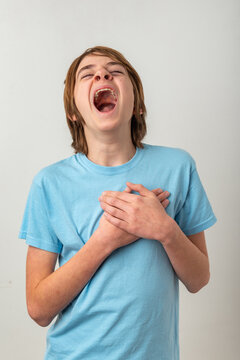 Young boy experiencing intense emotion, vocalizing loudly with an open mouth and closed eyes, expressing a deep feeling with hands crossed over his chest
