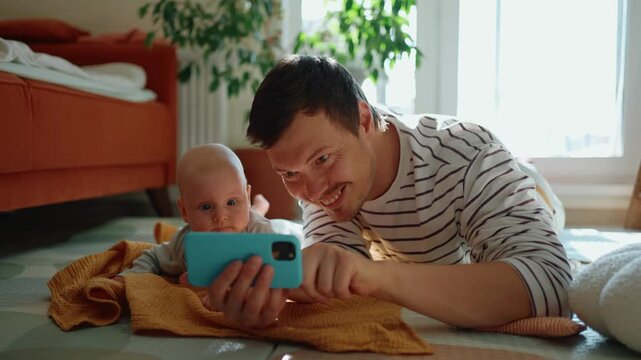 Young father showing his infant cartoons on a mobile phone, potentially overstimulating the child's fragile psyche and fostering early screen time dependence and addiction at home