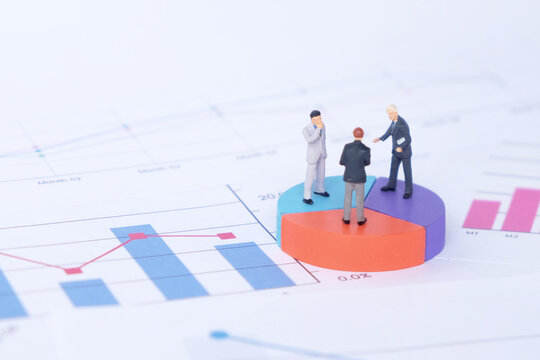 Miniature businessmen analyzing market trends on pie chart block with financial charts
