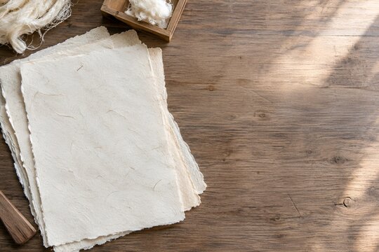 木の作業台に重ねた生成り色の手漉き和紙と楮繊維