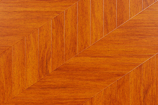 Texture di pavimento in parquet di legno color miele-ambrato, con motivo a spina di pesce chevron e venature naturali. Ideale come sfondo elegante per interni.