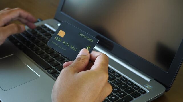 Man Holding Credit Card and Typing on Laptop for Online Shopping