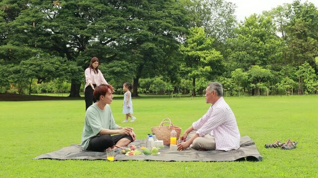Happy mother and daughter, Happy Asian family having fun time on picnic at city nature park sunny day, outdoor activitie with daughter father, mother and grandfather