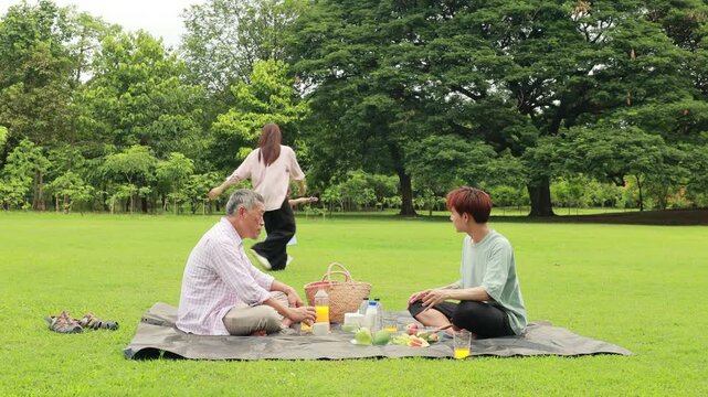 Happy mother and daughter, Happy Asian family having fun time on picnic at city nature park sunny day, outdoor activitie with daughter father, mother and grandfather