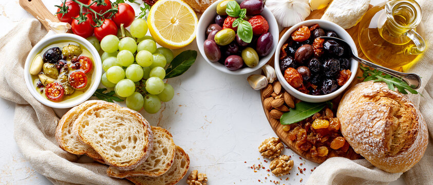 A vibrant spread of Mediterranean delights, featuring olives, grapes, tomatoes, lemon, nuts, and crusty bread, artfully arranged on a rustic board, promising a feast for the senses