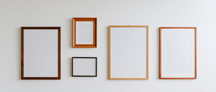 A collection of five empty picture frames of various sizes and colors hanging on a white wall, ready to be filled with artwork or photographs