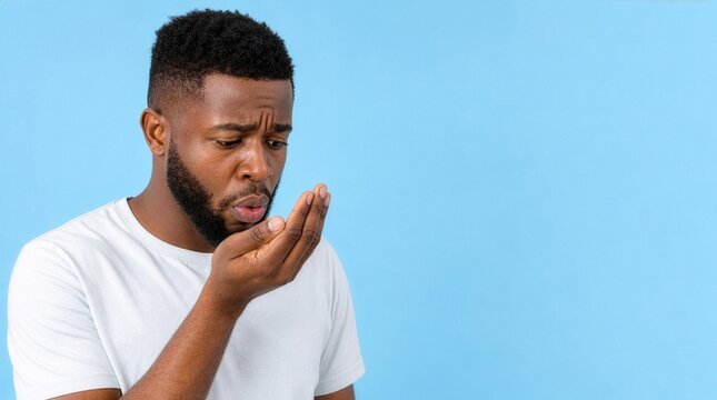 African American man checking bad breath on blue background