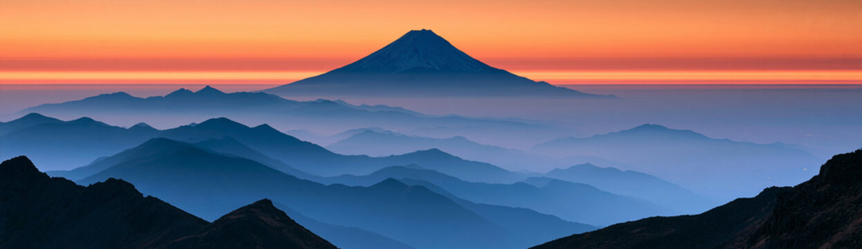 A majestic mountain peak emerges from a sea of mist, bathed in the warm glow of a setting sun. The layers of mountains recede into the distance, creating a sense of depth and tranquility