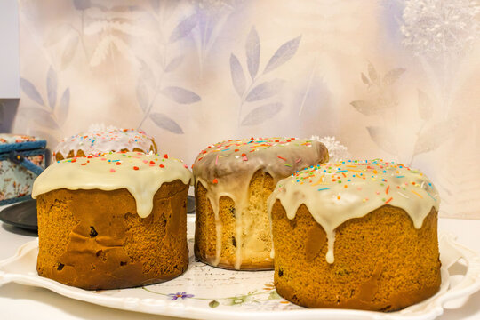 Three round glazed sweet breads with colorful sprinkles arranged on a decorative floral serving platter, featuring golden baked crusts and cream icing in a tabletop food scene and easter 