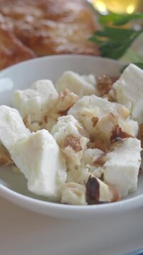 Close up of white goat cheese chunks with walnuts in ceramic bowl on breakfast table