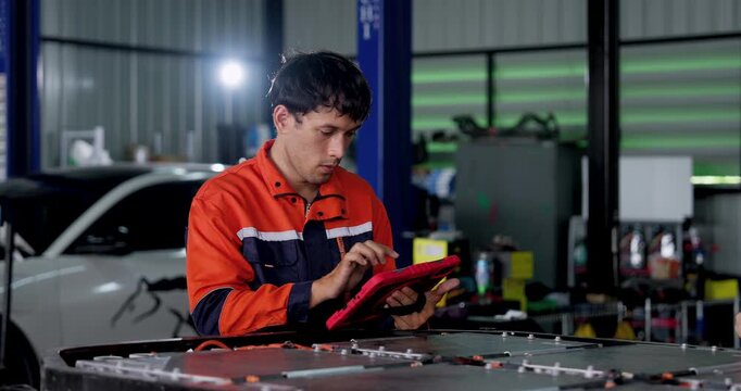 EV battery diagnostics in modern workshop: male technician taps and checks handheld testing device beside exposed battery pack, performing inspection during electric vehicle maintenance service.